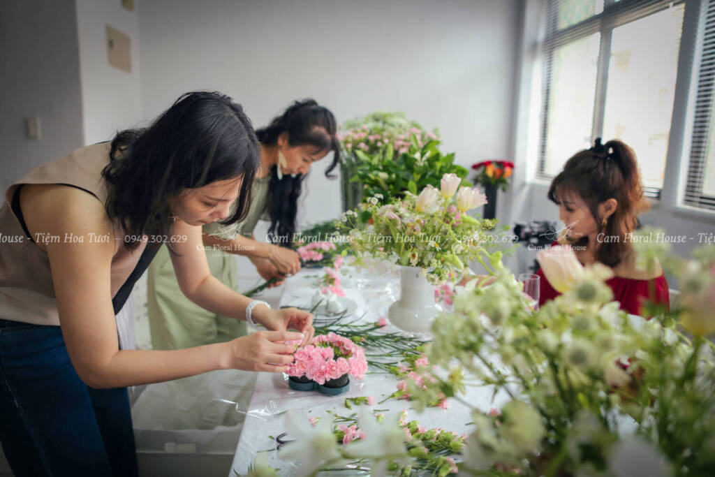 Several beautiful Asian women are attending a floral art class and diligently arranging flowers to complete their floral art pieces.